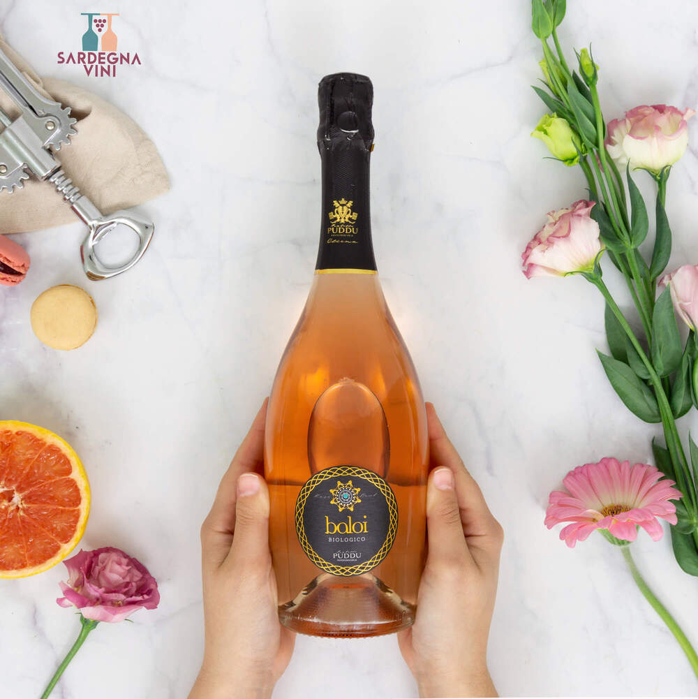 A bottle of Baloi Spumante Brut Rosé by Azienda F.lli Puddu with pink sparkling wine in a clear glass.